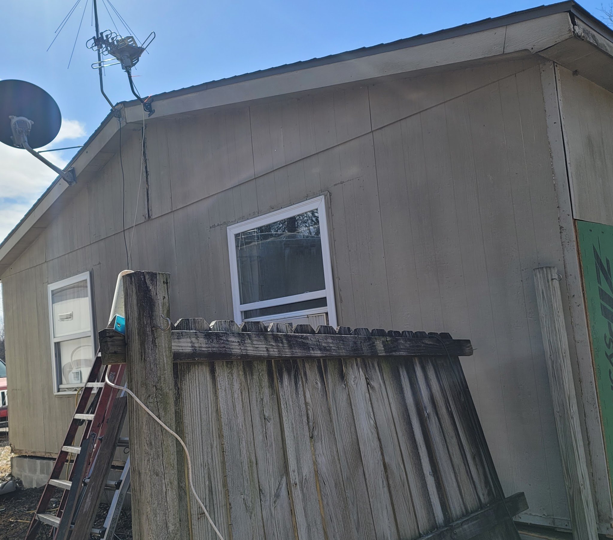 Leaning wooden privacy fence beside a house before repair