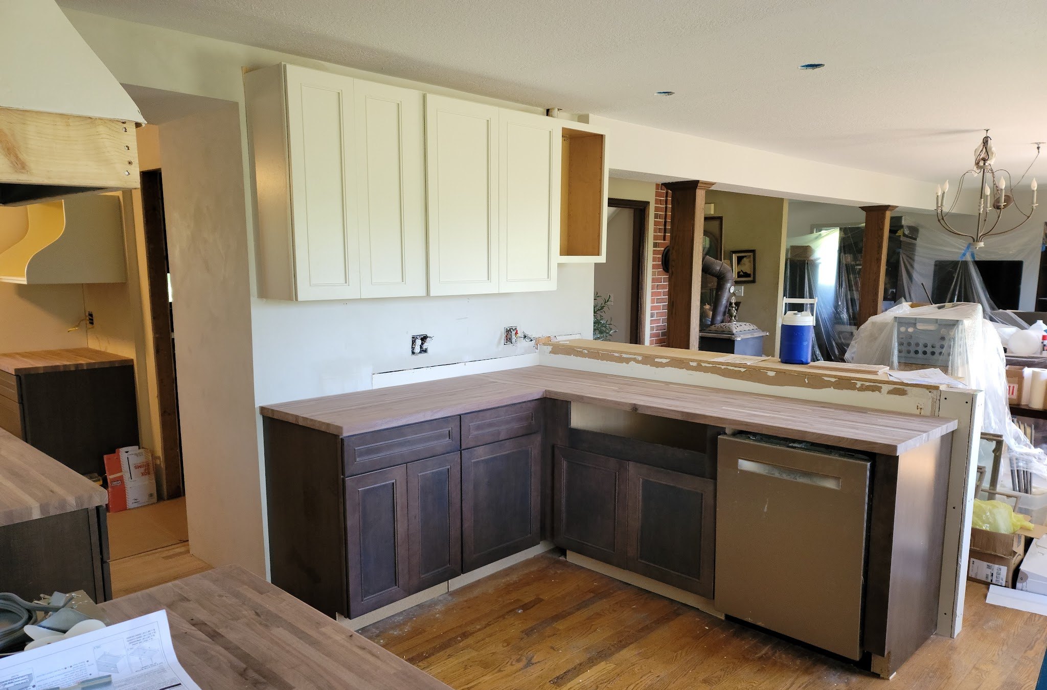 Kitchen during a remodel with dark lower cabinets, white uppers and butcher-block counters